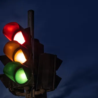 Feu de circulation avec les trois lumières allumées en rouge, jaune et vert contre un ciel nocturne.