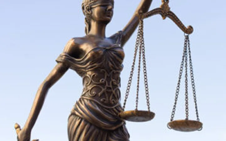 Bronze statue of Lady Justice holding a sword in her right hand and balance scales in her left, set against a clear blue sky.