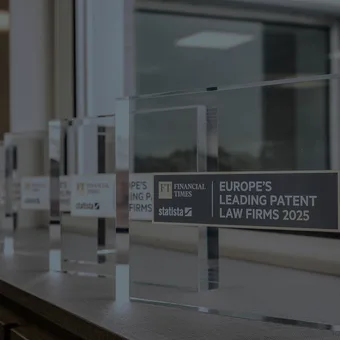 Row of transparent acrylic awards on a desk by a window; main plaque reads 'Europe's Leading Patent Law Firms 2025' with FT and Statista logos.
