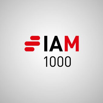 Portrait of a person in a navy blazer and white shirt, with short dark hair, against a grey gradient studio background.