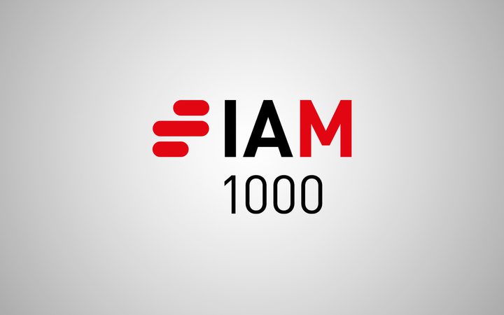 The logo features the text "I AM 1000" with a stylised red and black emblem resembling a speed or progress symbol on a grey background.