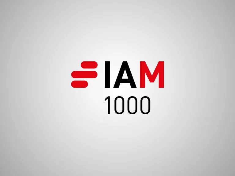 The logo features the text "I AM 1000" with a stylised red and black emblem resembling a speed or progress symbol on a grey background.