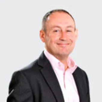 A professional person in a suit smiling at the camera against a plain white background.