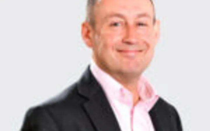 A man with a friendly smile, wearing a black blazer and white shirt, standing against a plain white background.