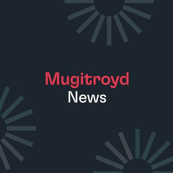 Dark blue graphic with the words Mugitroyd in red and News in white at the centre, surrounded by light teal radial burst motifs at the corners.