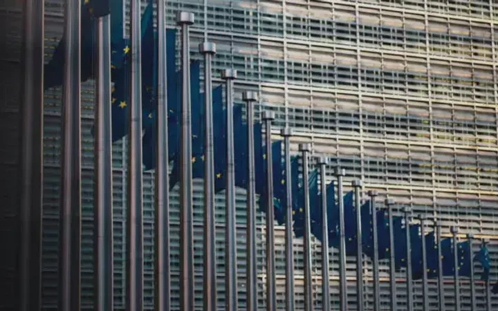 Multiple European Union flags on flagpoles in front of a modern glass building.