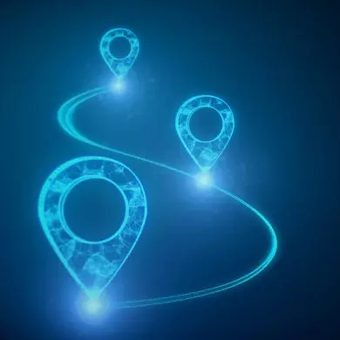 Portrait of a person with long dark wavy hair, wearing a blue top, smiling against a neutral grey backdrop.