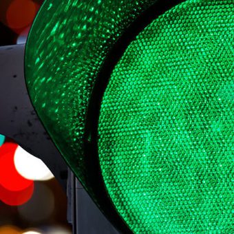 Close-up of a green traffic light with colourful blurred lights in the background.