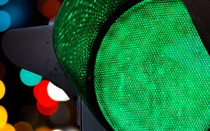 Close-up of a green traffic light with colourful blurred lights in the background.