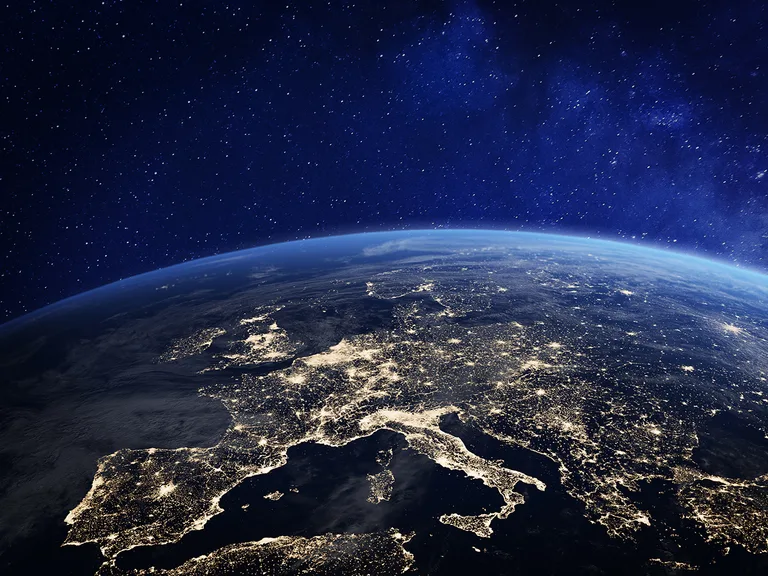 Earth seen from space at night, illuminated Europe and surrounding seas with many city lights, a bluish atmosphere rim, and a starry dark backdrop.