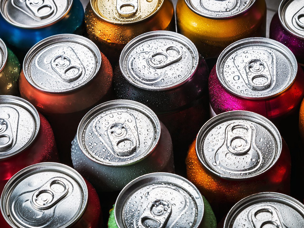 Close-up of colourful soda cans with condensation droplets and silver pull-tabs, viewed from above.
