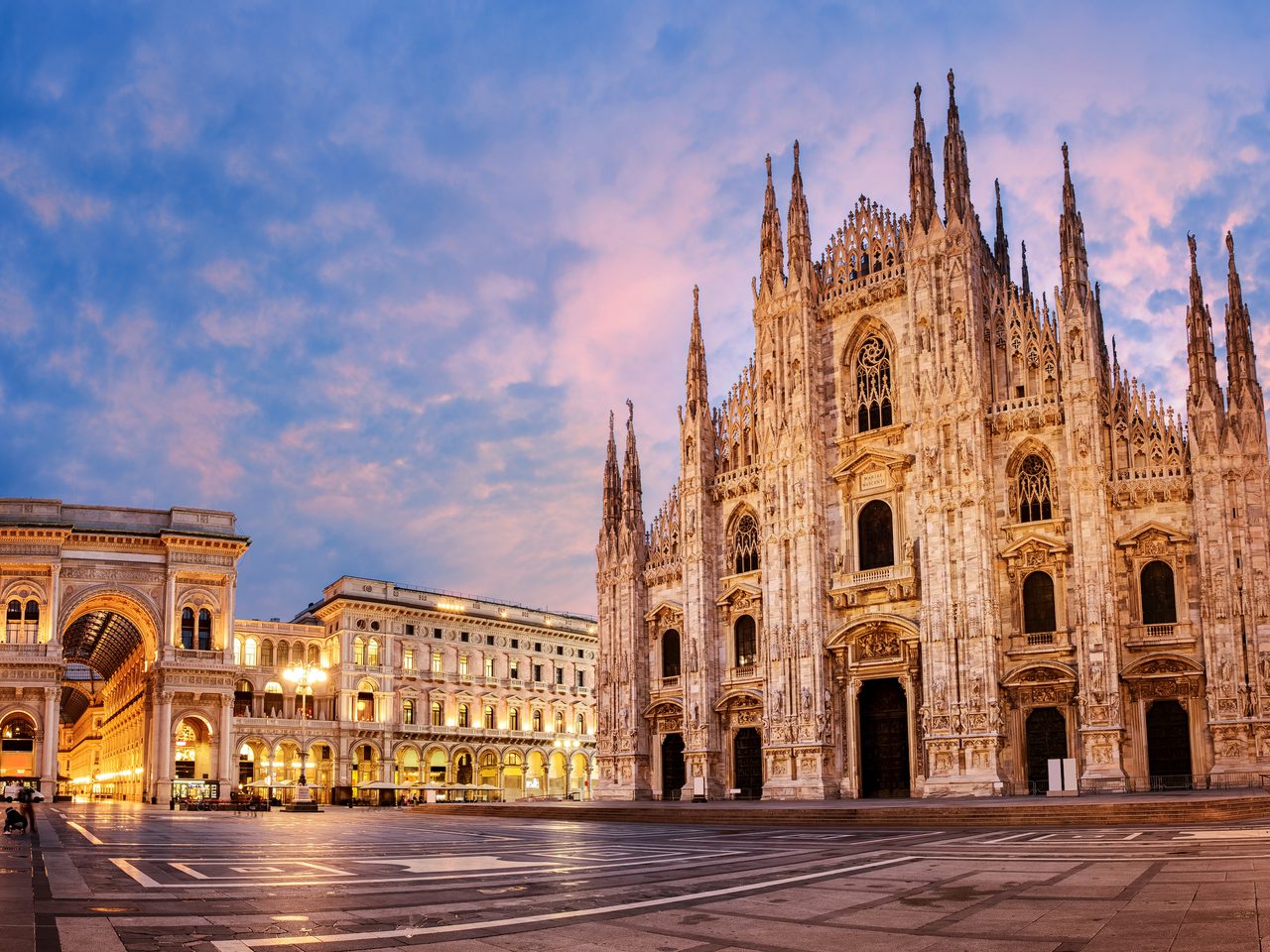 The Milan Cathedral (Duomo di Milano) in Piazza del Duomo at sunset, illuminated with a colourful sky and city lights.