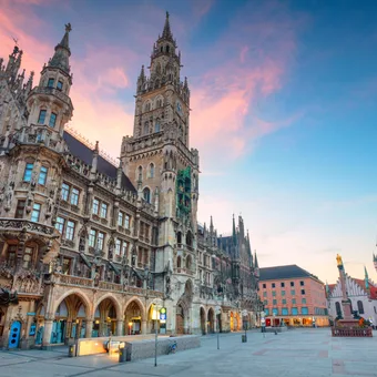 A historic Gothic-style building with ornate architecture and towers, set against a colorful evening sky in a spacious city square with few people.