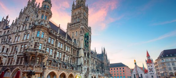 Historic city hall building with tall spires and ornate architecture in a large open square at sunset.