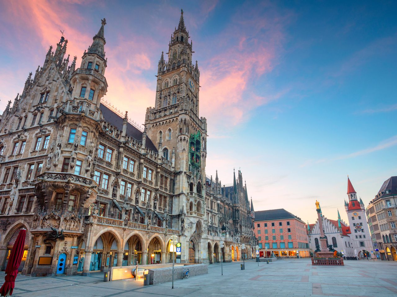 Historic Gothic-style building with tall spires and detailed facade in a spacious city square during sunset.