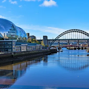Modern glass building and arches bridge over a river on a bright, sunny day with blue sky and reflections in the water.