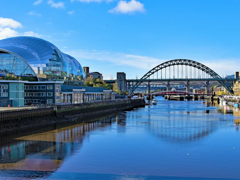 Modern glass building and arches bridge over a river on a bright, sunny day with blue sky and reflections in the water.