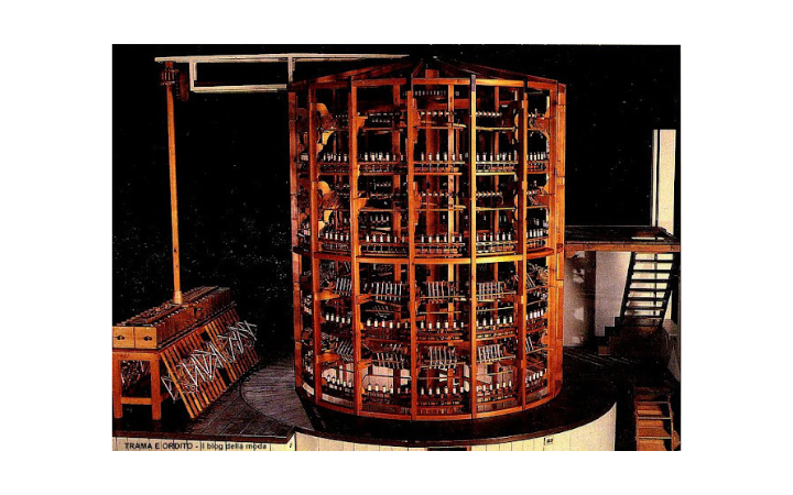 A large wooden structure with multiple shelves filled with bottles, resembling a wine rack, set in a room with a staircase and a small work area.