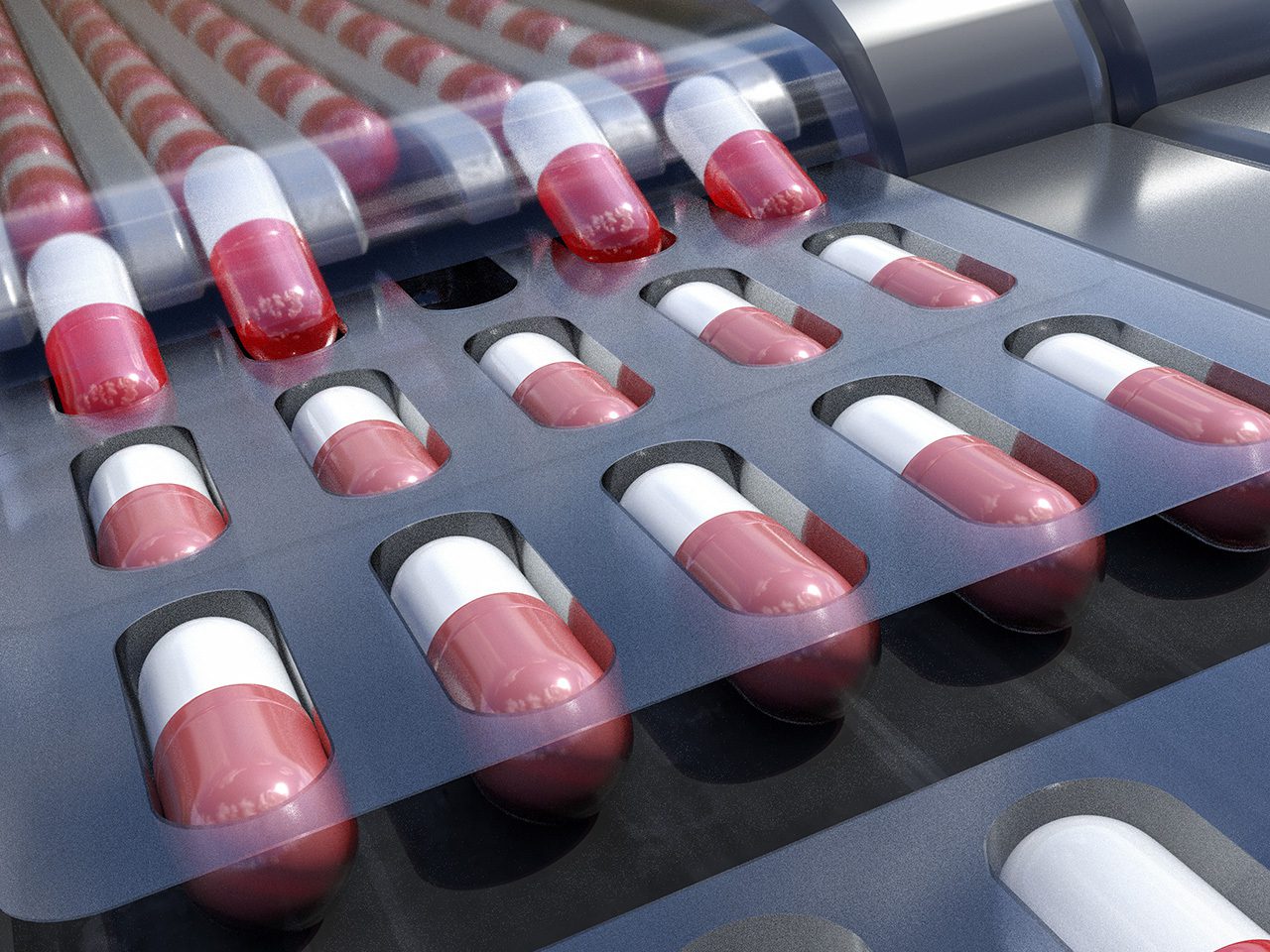 Medical capsules in a blister pack, mainly red and white, on a dark surface with reflections and a clear plastic cover at the top.