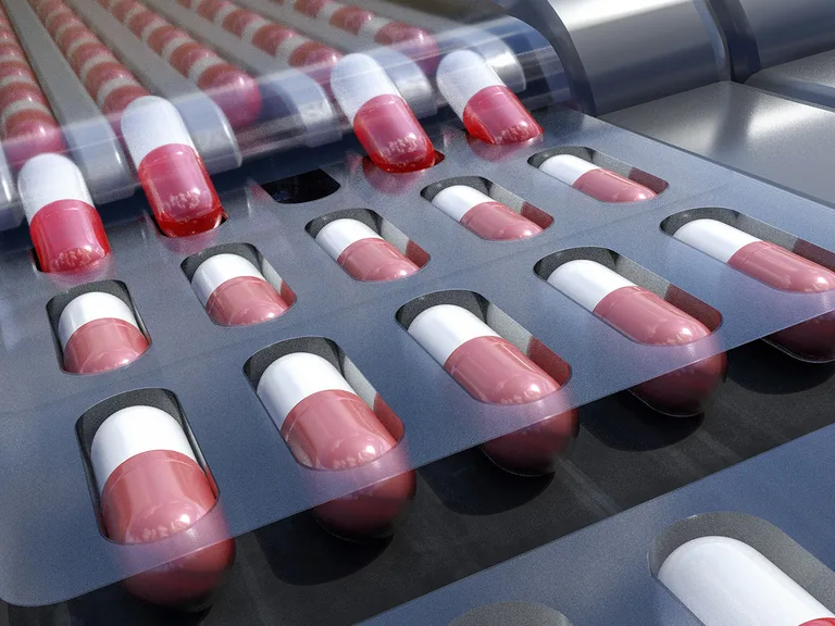 Medical capsules in a blister pack, mainly red and white, on a dark surface with reflections and a clear plastic cover at the top.