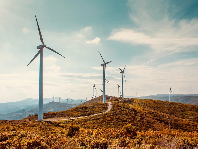 Wind turbines on rolling hills under a partly cloudy sky with autumnal vegetation in the foreground.
