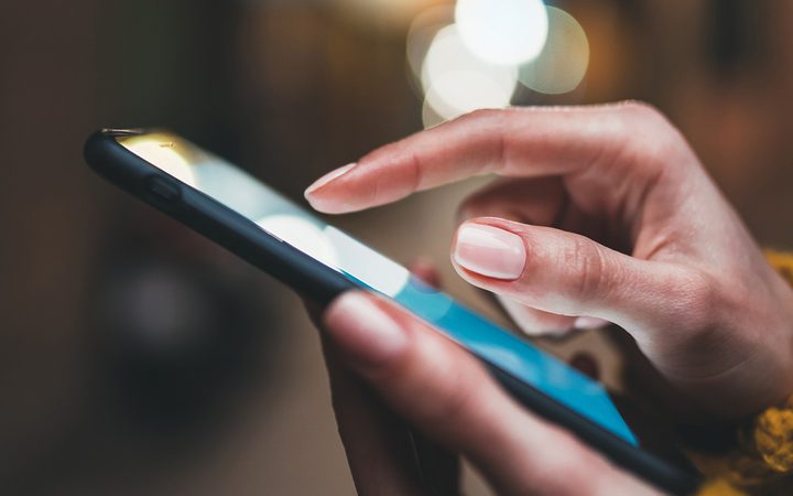 Close-up of a person's hand using a smartphone with a blurred background and bokeh light effects.