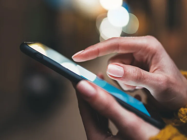 Close-up of a person's hand holding and using a smartphone with a blurred background and bokeh effect.