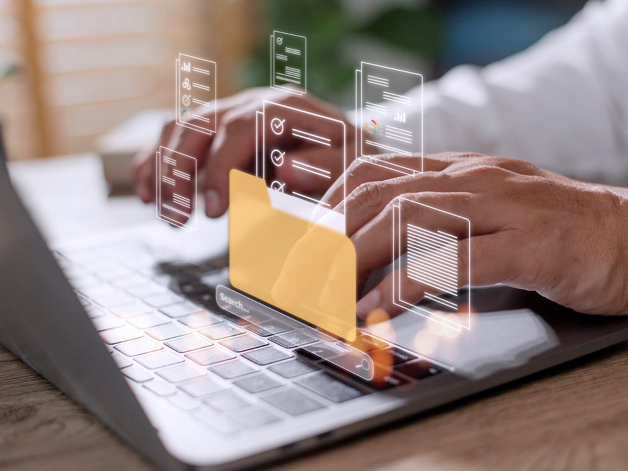 A person typing on a laptop with holographic, translucent documents and a yellow folder floating above the keyboard.