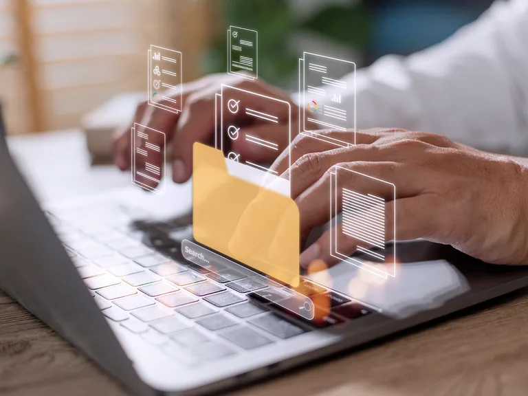 A person typing on a laptop with holographic, translucent documents and a yellow folder floating above the keyboard.