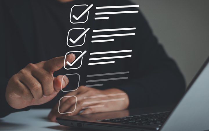 Person using a touchscreen with checkboxes and lists overlaid, interacting with a laptop in a modern, minimalistic setting.