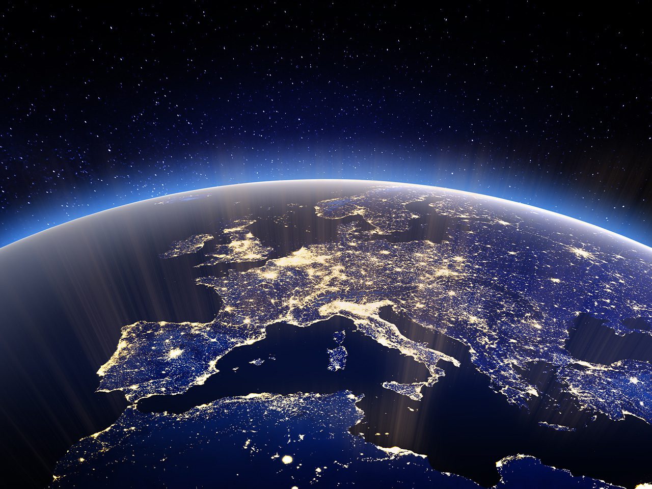 Earth from space at night, with Europe and nearby regions lit by city lights along the curved horizon, blue atmospheric glow and a starry dark sky.