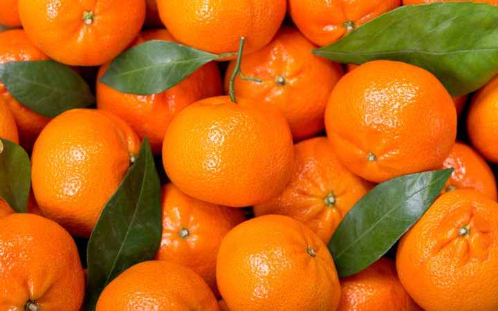 Close-up of a pile of bright, glossy oranges with a few green leaves scattered among them.