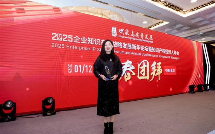 Woman in black dress holding an award, standing on stage in front of a large red backdrop at a professional conference.