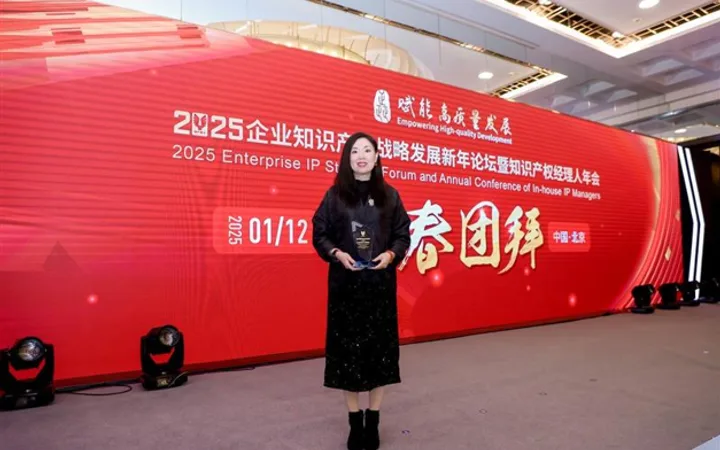 Woman in black dress holding an award, standing on stage in front of a large red backdrop at a professional conference.