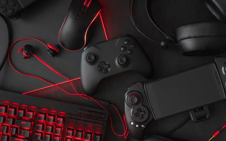 Dark desk setup with red LED gaming gear: keyboard, wired mouse, over-ear headset, black gamepad, handheld console, and red cables.