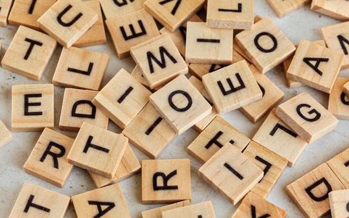 Scattered wooden letter tiles with black letters on a light background.