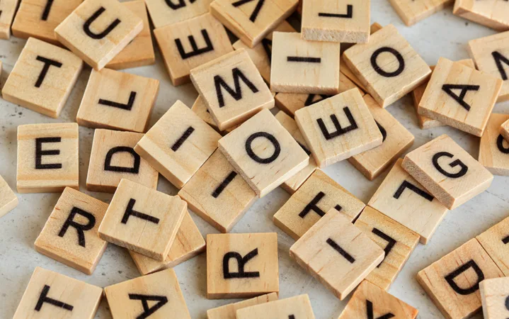 Scattered wooden Scrabble tiles with black letters on a light surface, some forming partial words, showing a random arrangement.
